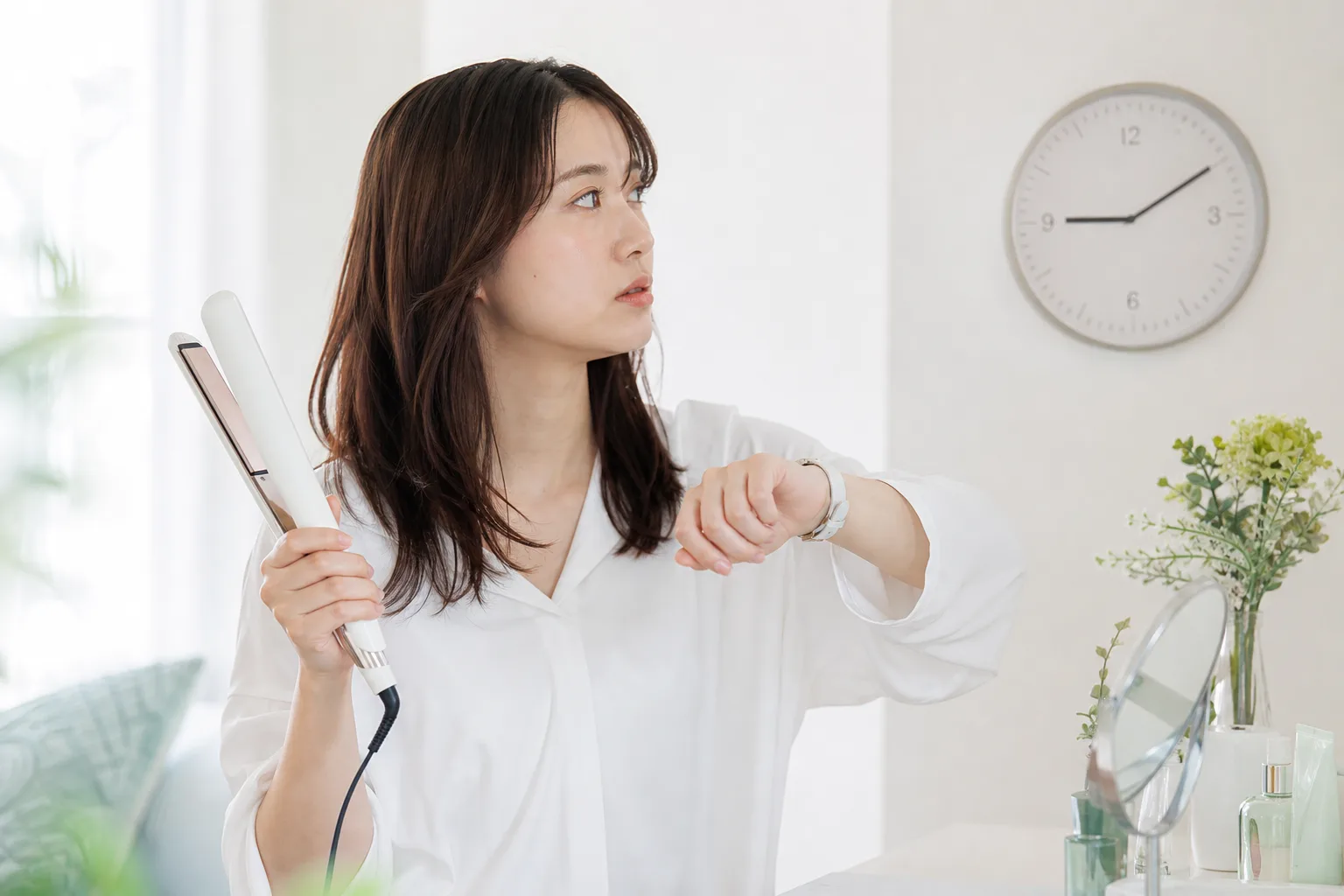 ヘアアイロンを持って時計を見る女性