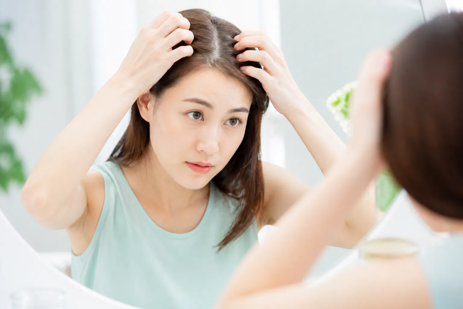 鏡で髪の根元と頭皮を確認する女性